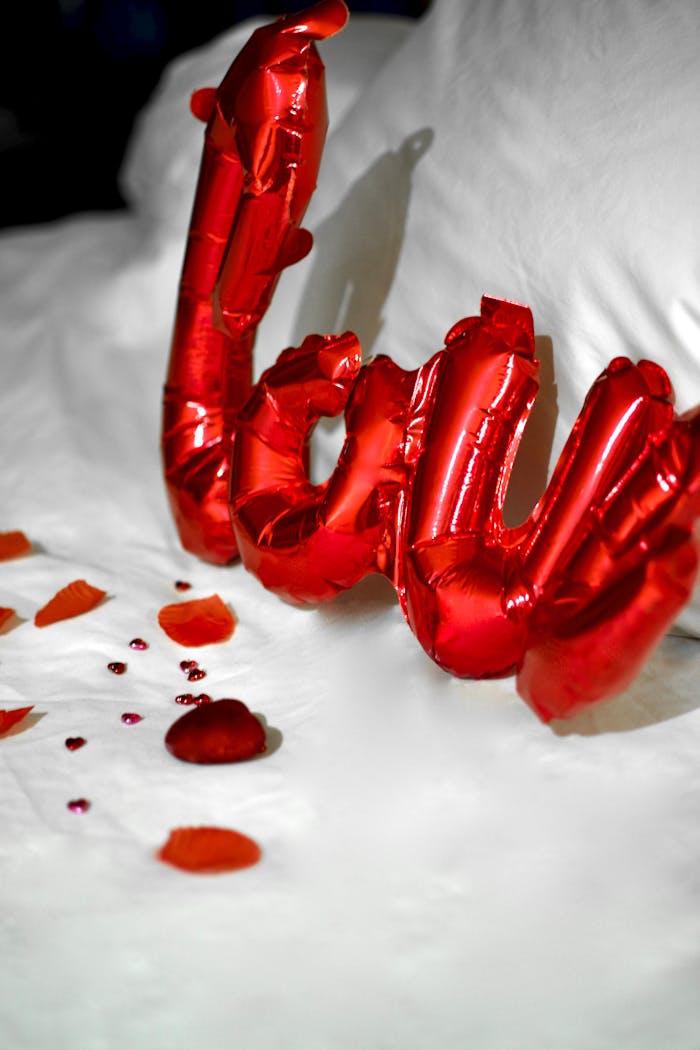 Red love balloons and rose petals on a white bed setting a romantic mood.