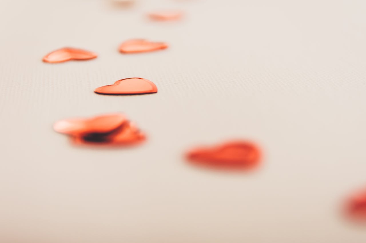 Red heart confetti scattered on a soft beige surface, perfect for Valentine’s Day or romantic themes.